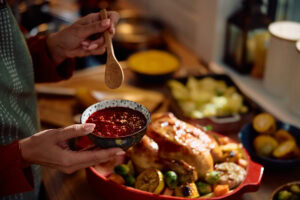 Lähikuva henkilöstä sekoittamassa kastiketta kanalle. Taustalla pöytä runsailla erilaisilla tarjoiluilla.