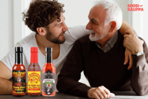 Isä ja poika hymyilevät toisilleen lämpimästi pöydän ääressä, heidän edessään on kolme chilikastikepulloa – Hellfire Fiery Fool, Dirty Dick’s Hot Sauce ja La Pimenterie The Forbidden Fruit.