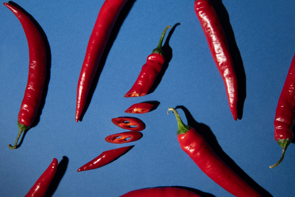 Punaisia kokonaisia ja viipaloituja chilejä sinisellä taustalla.