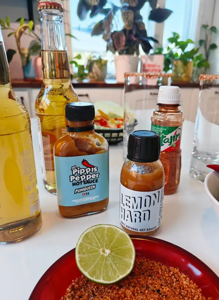 Micheladan ainekset pöydällä: lager, lime, Tajín-mauste ja Soosikaupan chilikastikkeet.