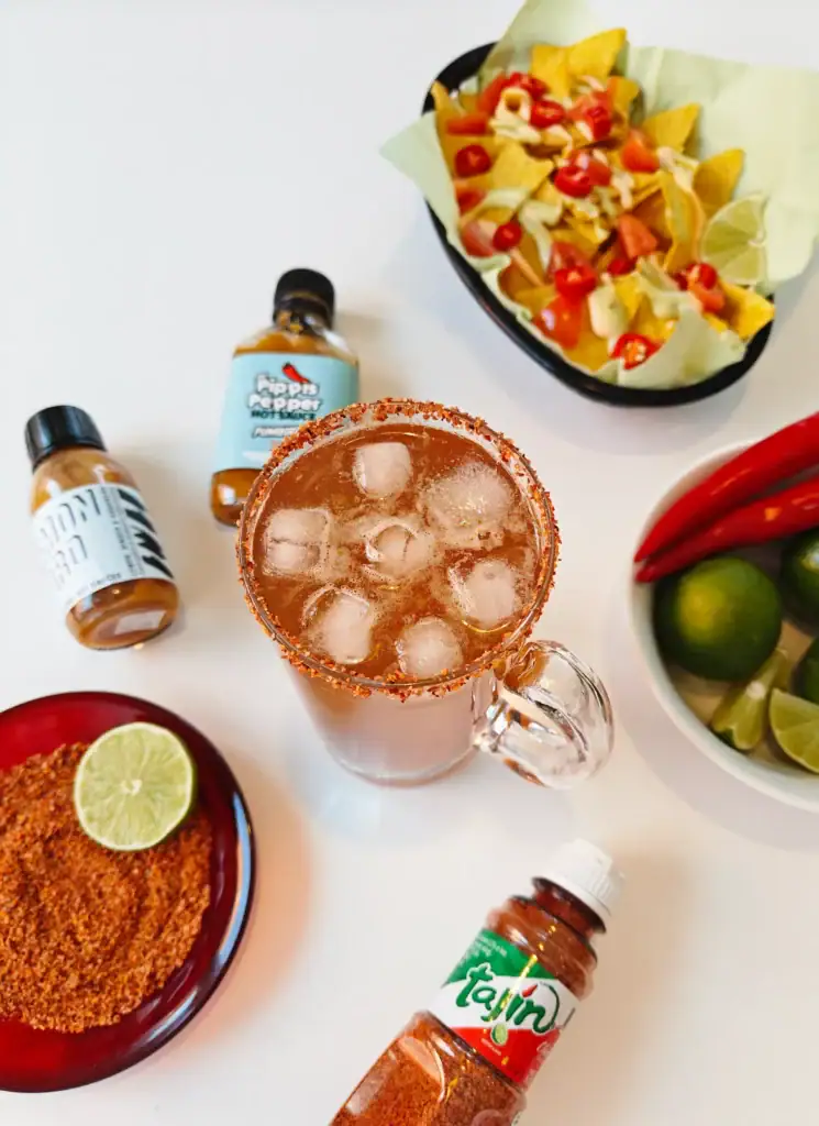 Michelada-olutdrinkki jääpaloilla ja Tajín-mausteella, tarjoiltuna limen ja soosikaupan  chilikastikkeiden kanssa.