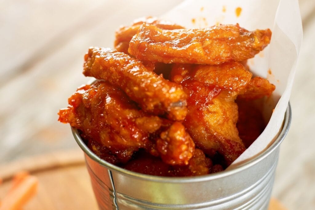 Buffalo wings in a metal serving dish with spicy buffalo sauce at the bottom.