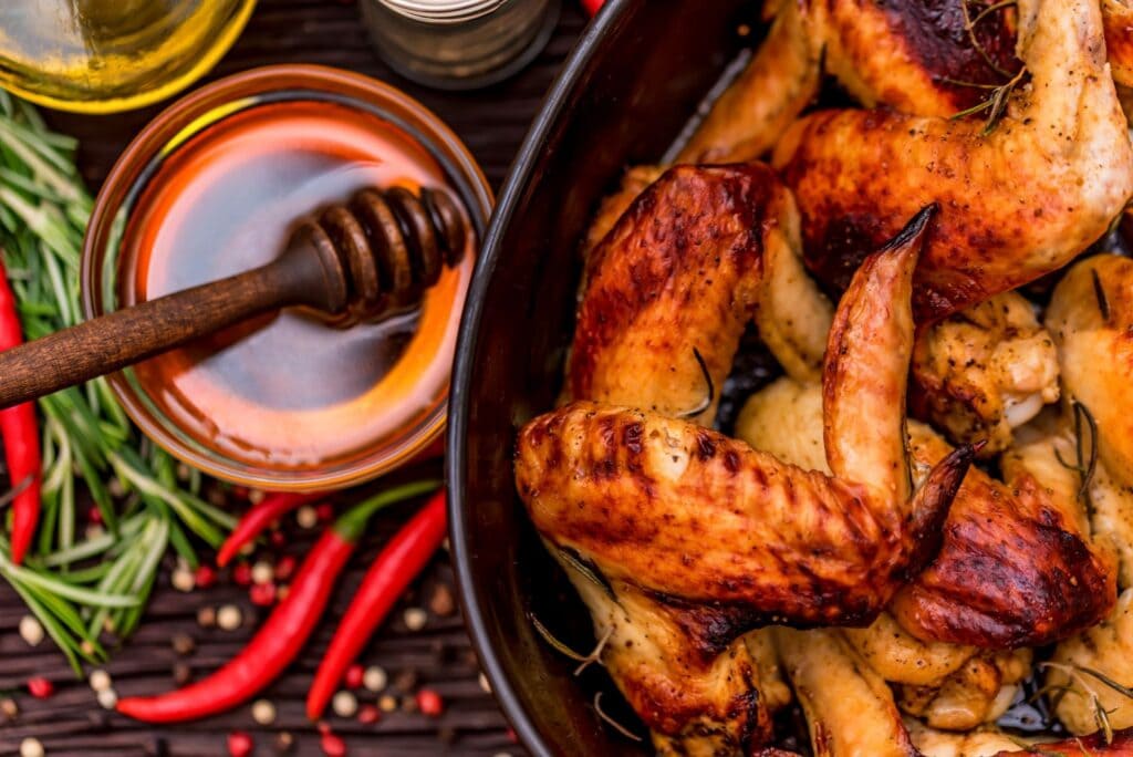 Chicken wings in a serving dish with honey and chilli on the side.