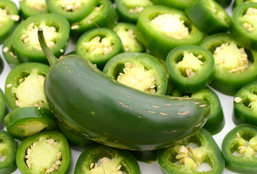 Kokonainen vihreä jalapeno viipaloitujen jalapenojen päällä. 